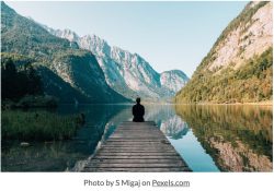 person sitting on the end of a dock on a lake